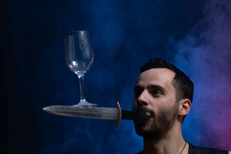 A man holds a knife in his mouth and keeping vine glass in balance. Unique circus skill.の写真素材
