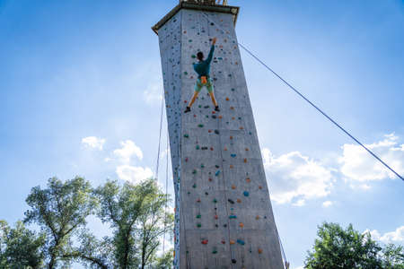 Sportsman climber training outdoor with blue sky , climbing on artificial colourful rock wall. Healthy lifestyle and bouldering concept.の写真素材