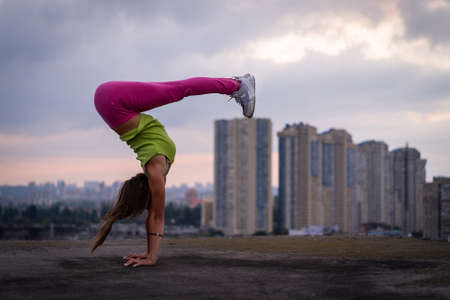 Flexible girl keep balance on hands on the cityscape background . Concept of creativity, balance and individualityの写真素材