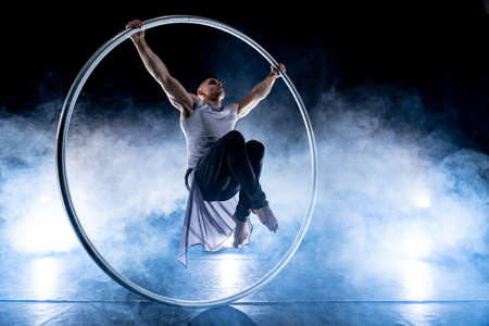 Cyr Wheel circus artist on smoked, dark background performing on stageの写真素材
