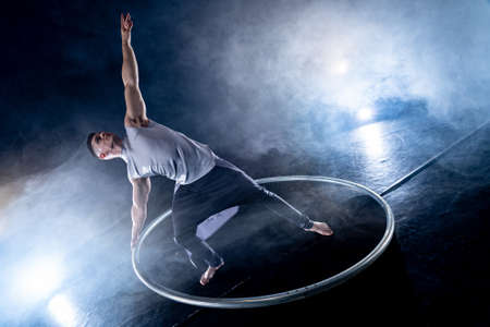 Cyr Wheel circus artist on smoked, dark background performing on stageの写真素材