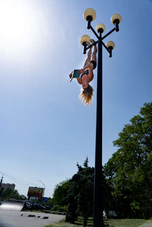 Girl hanging by feet upside down in the street on the Street light and reading book. Concept of combined knowledge, education and sport in the same timeの写真素材