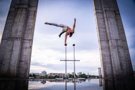 Flexible acrobat doing handstand on the cityscape background with columns on sides. Concept of willpower, control and dreamの写真素材