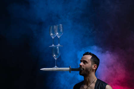Man hold knife in the mouth and keep in balance wineglasses on it. concentrationの写真素材