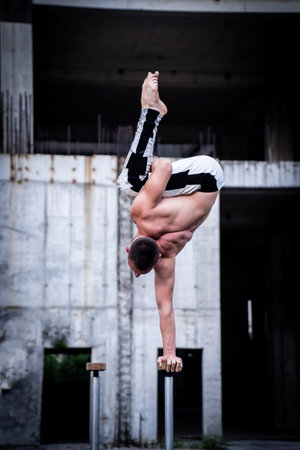 Man keeps balance on one hand on the concrete structure background. Concept of yoga, meditation and healthy lifestyleの写真素材