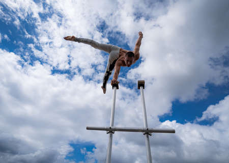 Flexible male circus Artist keep balance by one hand on the rooftop against amazing cloudscape. Motivation, passion and achievement conceptの写真素材