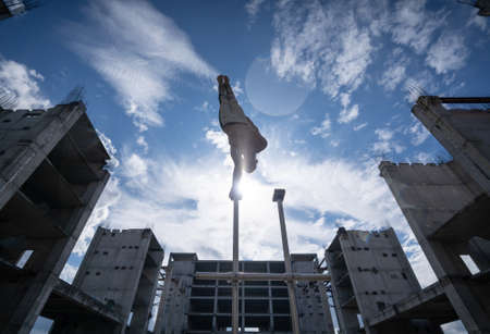 Circus artist keeps balance on one hand on the sky and industrial construction background. Concept of handstand, performing and artの写真素材