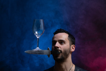 A man holds a knife in his mouth and keeping vine glass in balance. Unique circus skill.の写真素材