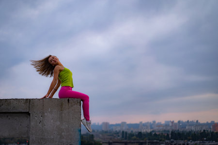 Silhouette of woman sitting on the edge on the dramatic cloudscape during sunset with cityscape on background. concept of excitement, emotion and happinessの写真素材