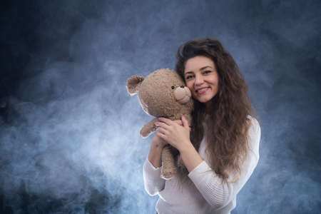 cheerful curly young woman holding teddy bear. concept of present and happinessの写真素材