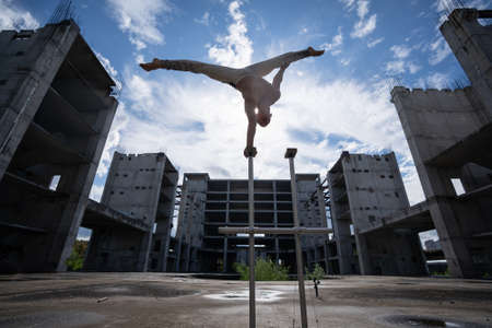 Circus artist keeps balance on one hand on the sky and industrial construction background. Concept of handstand, performing and artの写真素材