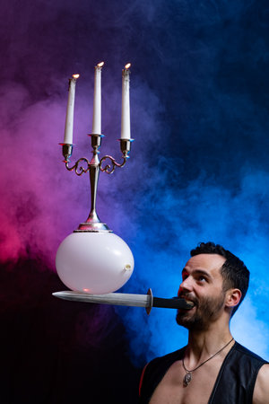 A circus artist holds a knife in his mouth a balloon with a candelabrum and burning candles on it and keeps it in balanceの写真素材