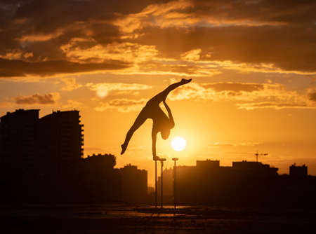 Flexible female circus Artist keep balance and doing contortion on the rooftop against dramatic sunset and cityscape. Motivation, passion and achievement conceptの写真素材