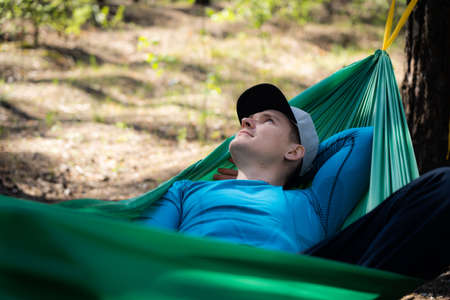 Young happy man in hat relaxing outside in hammock in forest.の写真素材