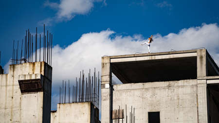 Flexible woman keep balance on one foot on the edge of building under construction. Risk, courage and chance conceptの写真素材