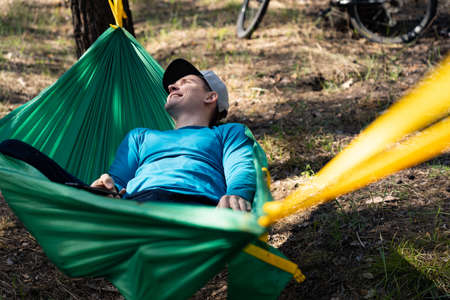 Young happy smiling man in hat relaxing outside in hammock in forest.の写真素材