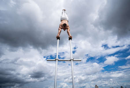 Flexible male circus Artist keep balance on the hands against amazing cloudscape. Individuality, outstanding and originality.の写真素材