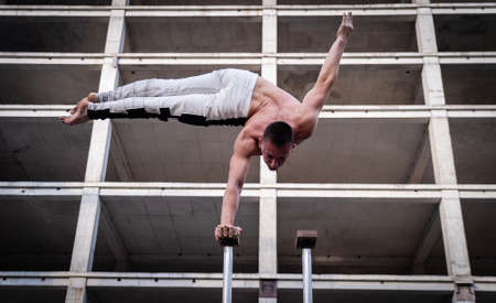 Flexible acrobat doing handstand on the industrial construction background with columns on sides. Concept of willpower, control and dreamの写真素材