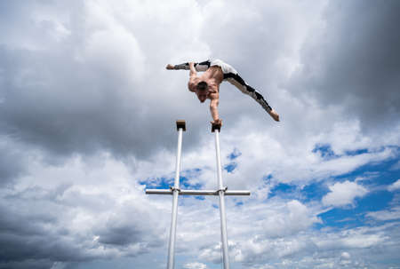 Flexible male circus Artist keep balance by one hand on the rooftop against amazing cloudscape. Motivation, passion and achievement conceptの写真素材