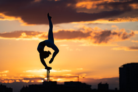 Flexible female circus Artist keep balance and doing contortion on the rooftop against dramatic sunset and cityscape. Motivation, passion and achievement conceptの写真素材