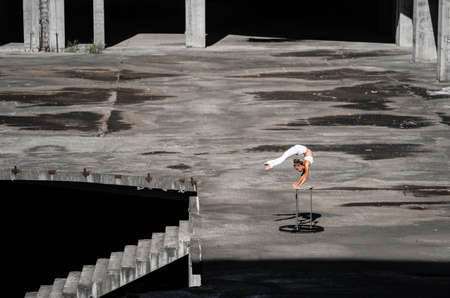 Flexible and fit girl standing on her hands keeping balance in the abandoned building. Concept of effort, self-development and healthy lifestyleの写真素材