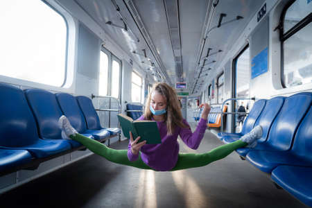 Very flexible wearing mask woman reading book in the subway car sitting in the gymnastic split. Concept of healthy lifestyle, flexibility and yogaの写真素材