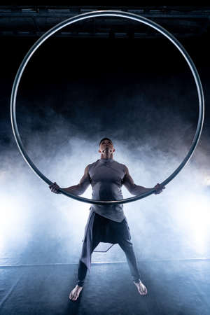 Cyr Wheel circus artist on smoked, dark background performing on stageの写真素材