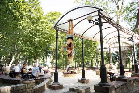 14 of February 2020, Kiev, Tarasa Shevschenka square. Girl hanging by feet upside down in the park and reading book. Concept of education and self-developmentのeditorial素材