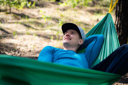 Young happy man in hat relaxing outside in hammock in forest.の写真素材
