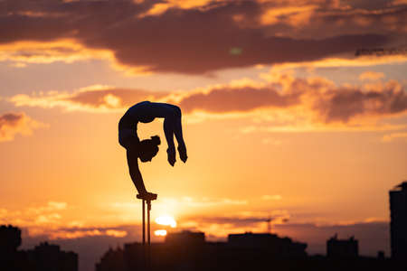 Silhouette of flexible and fit girl doing handstand and keeping balance against dramatic unset. Concept of yoga and healthy lifestyleの写真素材