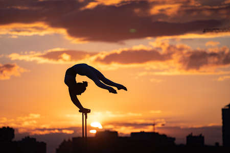 Flexible female circus Artist keep balance and doing contortion on the rooftop against dramatic sunset and cityscape. Motivation, passion and achievement conceptの写真素材