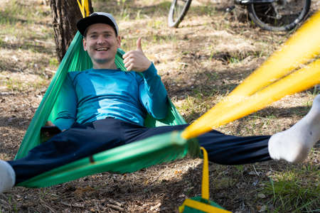 Young happy smiling man in hat relaxing outside in hammock in forest.の写真素材