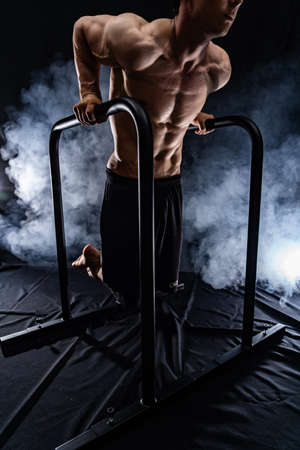 Muscular build man doing crossfit on parallels bar indoor on black, smoked background. concept of healthy lifestyle and calisthenicの写真素材