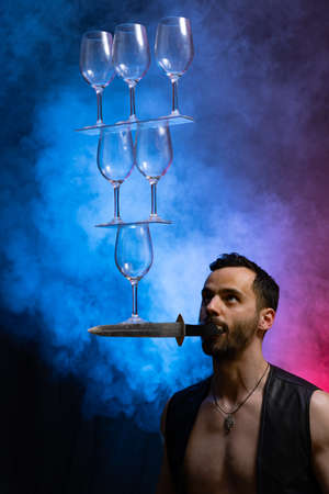 Man hold knife in the mouth and keep in balance wineglasses on it. concentrationの写真素材