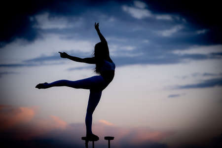 Silhouette of flexible and fit girl standing on fits with split and keeping balance against dramatic sky during sunset Concept of yoga and healthy lifestyleの写真素材