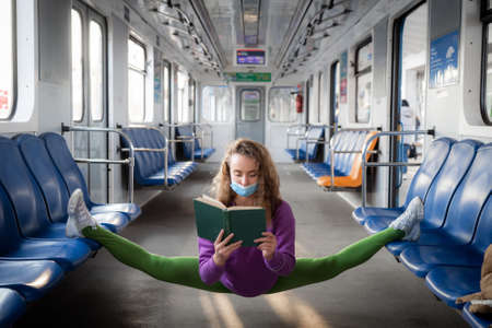 Flexible woman sitting on the split in the subway and reading book. Concept of education and self-development during COVID and quarantineの写真素材