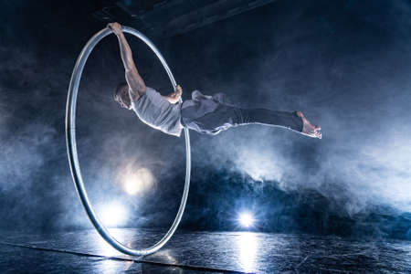Cyr Wheel circus artist on smoked, dark background performing on stageの写真素材