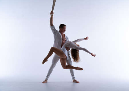 Aerial straps duo wearing white costume on white background doing performance in slow motion. Concept of romantic relation ship in coupleの写真素材