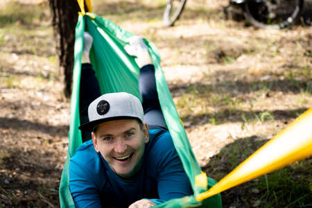 Young happy smiling man in hat relaxing outside in hammock in forest.の写真素材