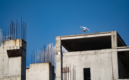 Flexible female circus artist keep balance on one hand on the edge of building under construction. Motivation, passion and achievement conceptの写真素材