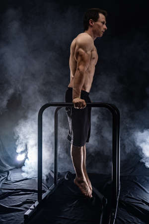 Muscular build man doing calisthenics on parallels bar indoor on black, smoked background. concept of motivation, desire and passionの写真素材