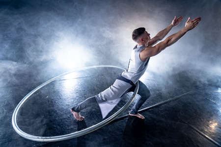 Cyr Wheel circus artist on smoked, dark background performing on stageの写真素材
