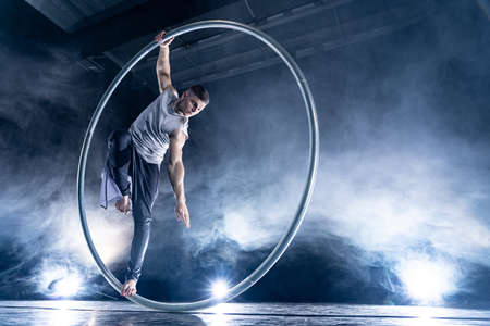 Cyr Wheel circus artist on smoked, dark background performing on stageの写真素材