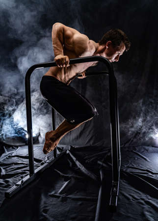 Muscular build man doing calisthenics on parallels bar indoor on black, smoked background. concept of healthy lifestyle and powerの写真素材