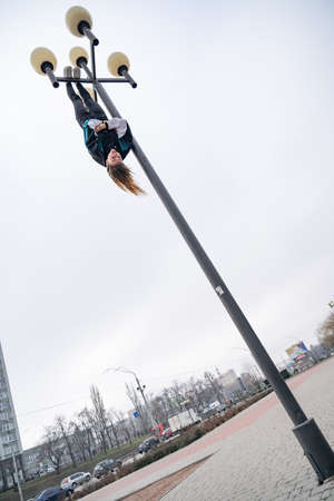 Young attractive Girl hanging by feet upside down on the street light in the street. super extreem. concept of courage and meditationの写真素材