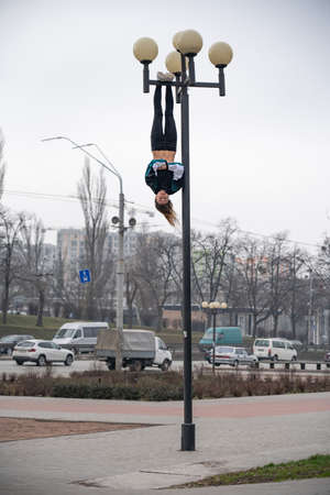 Young attractive Girl hanging by feet upside down on the street light in the street. super extreem. concept of courage and meditationの写真素材