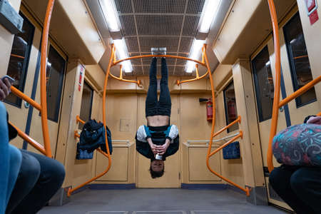 Girl hanging by feet upside down in the subway carriage and using smartphone. Concept of overusing social networks and addictionの写真素材