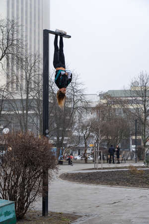 Young attractive Girl hanging by feet upside down on the street light in the street. super extreem. concept of courage and meditationの写真素材