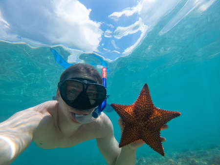Caucasian man holding and showing starfish during snorkeling underwaterの写真素材