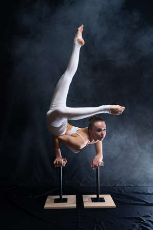 Flexible circus artist - female acrobat doing handstand on the back and smoker background. concept of willpower and passion.の写真素材